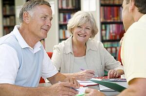 Three people in library writing in notebooks (selective focus)
