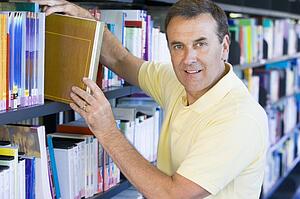 Man in library pulling book off a shelf (depth of field)