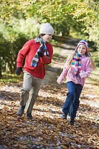 Two young children running on path outdoors smiling (selective focus)