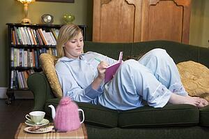 Young woman lying on sofa at home writing in her diary