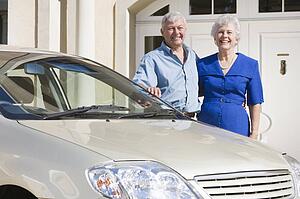 Senior couple standing with their car outside their home