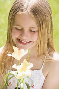 Young girl standing outdoors holding blossom smiling