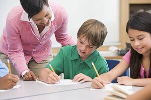 Students in class writing with teacher helping