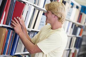 Man in library pulling book off a shelf (depth of field)