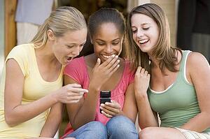 Teenage Girls Sitting Outside Playing With Mobile Phone