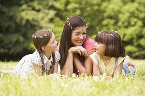 Mother and daughters lying outdoors with flowers smiling