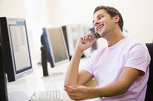 Man sitting in computer room using cellular phone and smiling