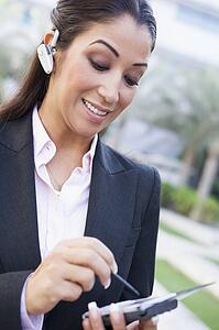 Woman wearing headset outdoors and using personal digital assistant smiling (selective focus)