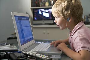 Young boy in bedroom using laptop and listening to MP3 player