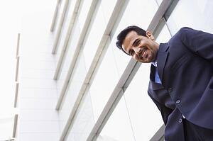Businessman standing outdoors by building smiling (high key/selective focus)