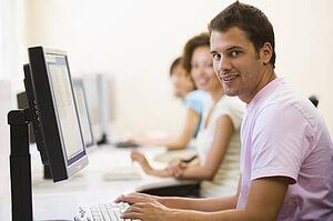 Three people sitting in computer room typing and smiling