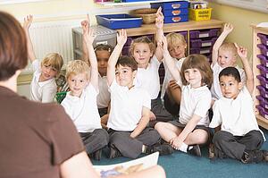 Students in class sitting on floor volunteering for teacher (selective focus)