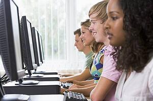 Four people sitting at computer terminals (selective focus/high key)