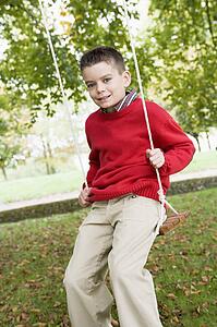 Young boy outdoors on tree swing smiling (selective focus)