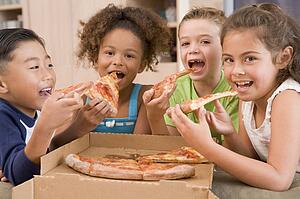 Four young children indoors eating pizza smiling