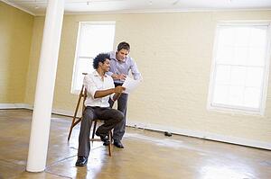 Two men with ladder in empty space looking at paper