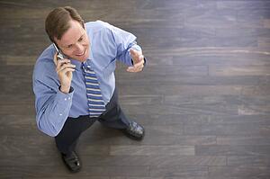 Businessman standing indoors using cellular phone and smiling