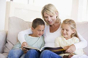 Woman and two children sitting in living room reading book and smiling