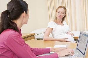 Doctor with laptop and pregnant woman in doctor's office smiling