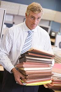 Businessman standing in cubicle with stacks of files