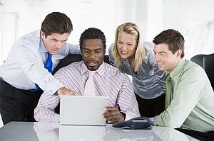 Four businesspeople in a boardroom pointing at laptop and smiling