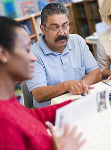 Three people sitting in library with books and notepads (selective focus)