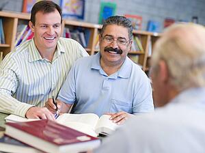 Two men sitting in library near another man with a book and notepad (selective focus)