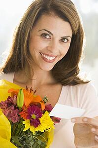 Woman holding flowers and note smiling