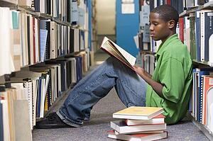 Man sitting on floor in library reading book