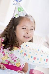 Young girl wearing party hat looking at birthday cake smiling