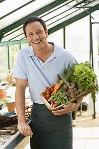 Man in greenhouse holding basket of vegetables smiling