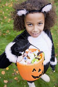 Young girl outdoors in cat costume on Halloween holding candy
