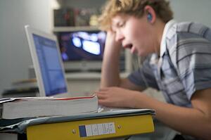 Young boy in bedroom yawning using laptop and listening to MP3 player
