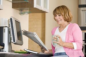 Woman in kitchen with newspaper and coffee smiling