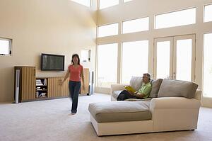 Man reading book in living room with woman walking by