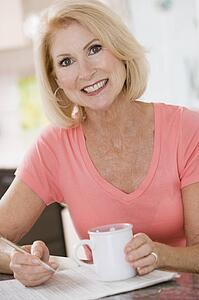 Woman in kitchen with coffee and newspaper smiling