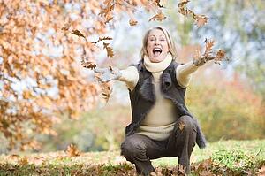Woman outdoors throwing leaves up and smiling (selective focus)