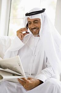Man sitting indoors with newspaper and cellular phone smiling (high key/selective focus)