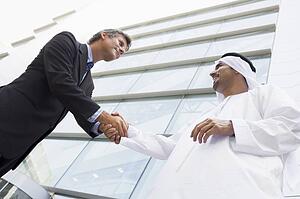Two businessman outdoors by building shaking hands and smiling (high key/selective focus)