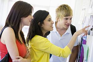 Three students in corridor looking at bulletin board (high key)