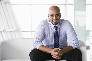Businessman sitting indoors smiling (high key/selective focus)