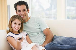 Man and young girl in living room with remote control smiling