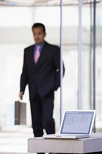 Laptop sitting on stone bench outdoors with businessman walking in background (high key/selective focus)