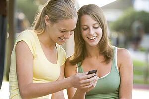 Teenage Girls Sitting Outside Playing With Mobile Phone