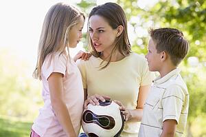 Woman and two young children outdoors holding volleyball and smiling