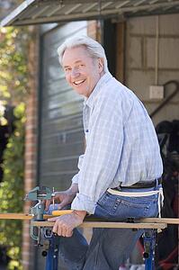 Man at shed sitting on tool bench smiling