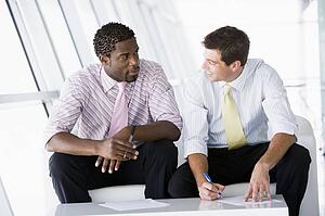 Two businessmen sitting in office lobby talking and smiling
