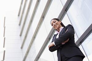 Businesswoman standing outdoors by building smiling (high key/selective focus)