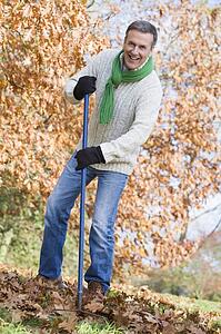 Man outdoors raking leaves and smiling (selective focus)