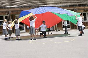 Students outdoors during recess playing with a parachute